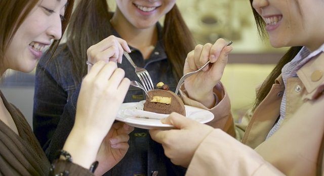 mulheres japonesas segurando juntas um prato. Todas com o garfo na mão compartilham um pedaço de bolo. Vontade de comer doces